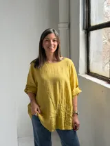 Blusa mostaza de lino, con cuello redondo, mangas tres cuartos con presilla y botón, y detalle de pliegues en la parte inferior.