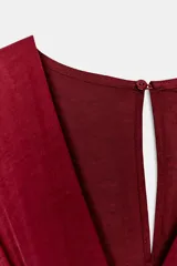Mono largo satinado de color rojo, con escote en V cruzado y manga corta. Presenta cintura elástica con cinturón negro incorporado, bolsillos laterales ocultos y terminación de las piernas con puño elástico.