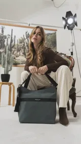 Cartera tipo hobo de tamaño grande en color beige, con detalles en negro. Presenta una franja horizontal negra con el logo de la marca, asa corta de hombro y correa larga desmontable. Incluye bolsillo frontal con cierre oculto y bolsillo trasero.