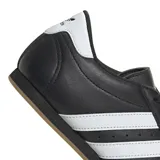 Championes Adidas modelo Taekwondo Lace, de diseño minimalista en color negro con las tres tiras características en blanco y detalle en el talón. Presentan una silueta de perfil bajo con costuras reforzadas en la puntera y suela de goma color caramelo.