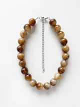 Collar de cuentas esféricas grandes con diseño marmolado en tonos marrones y beige, con cadena de extensión metálica plateada.