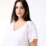Remera blanca con cuello en V y mangas cortas adornadas con detalles bordados tipo broderie y perforaciones geométricas.