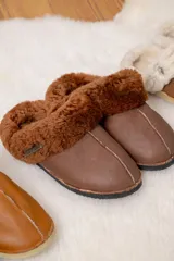 Pantufla de cuero color habano con interior de piel sintética, suela de goma y detalle de costura central.