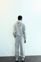 Pantalón jogger gris melange de tiro medio con cintura elástica y puños elásticos en los tobillos. Presenta bolsillos laterales ocultos y un estampado frontal con la palabra "LOS ANGELES" en azul marino.