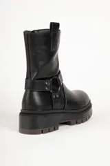 Bota estilo biker de cuero sintético color negro, con suela tipo plataforma dentada. Presenta una tira decorativa con argolla metálica y apliques de tachas en el tobillo.