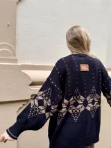 Saco de punto gris con diseño geométrico en color amarillo, cierre frontal con botones, cuello redondo y bordado de corazón pequeño en el pecho.