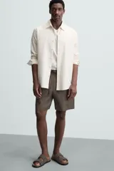 Bermuda de lino color blanco hueso, de corte relajado y tiro medio. Presenta cintura elástica ajustable con cordón, pliegues frontales y bolsillos laterales y trasero.