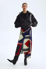 Pollera larga con diseño cruzado efecto pañuelo y brillo sutil. Presenta un estampado geométrico multicolor en tonos azul, rojo y crudo con detalles de cadenas.