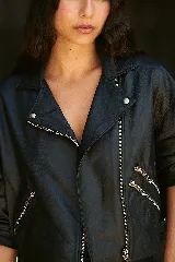 Chaqueta de cuero ovino negra, estilo biker, con cuello con solapa, cierre frontal asimétrico con cremallera, mangas globo con puños ajustables con cremallera y cinturón con hebilla en la cintura.