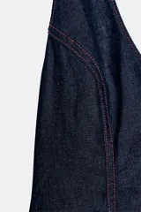 Top de mezclilla (denim) azul oscuro con cuello halter que se anuda en la espalda, escote pronunciado en pico y bajo abullonado con elástico. Presenta pespuntes contrastantes en color rojo.