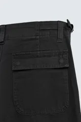 Pantalón de corte recto confeccionado en tejido de algodón con estructura diagonal. Presenta cintura ajustable en los laterales con trabillas, bolsillos delanteros tipo cargo y bolsillos traseros con solapa. Cierre frontal con cremallera y botón.