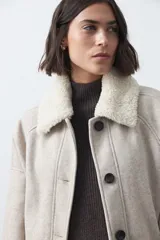 Campera corta de paño color gris con cuello de corderito blanco, cierre frontal con botones y bolsillos laterales.