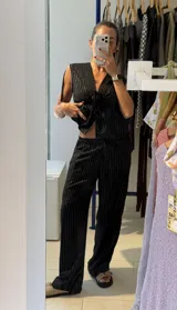 Pantalon negro de corte holgado con estampado de rayas verticales finas en hilo brillante. Posee cintura elastizada con cordón de ajuste frontal.