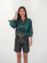Camisa negra de satén con brillo satinado, escote en V, mangas largas y botones de nácar. Cuenta con cordones laterales ajustables para fruncir la prenda.