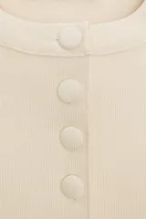 Chaqueta entallada azul marino de punto, con cuello redondo y mangas cortas abullonadas con aberturas. Cierre frontal con botones forrados a tono.