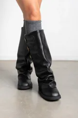 Botas de caña alta confeccionadas en cuero negro, con diseño holgado y tres correas horizontales con hebillas metálicas doradas en la parte superior. Presentan punta redondeada y taco bajo cuadrado.