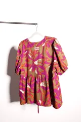 Blusa de calce holgado con estampado floral en tonos marrones, fucsias, naranjas y blancos. Tiene escote en V con doble lazo ajustable y mangas 3/4 con volumen.
