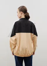 Campera de tela avión con diseño color block en negro y verde, con detalles de franjas blancas en las mangas. Presenta cierre frontal completo, cuello alto, puños y ruedo elásticos, y logo bordado en el pecho.