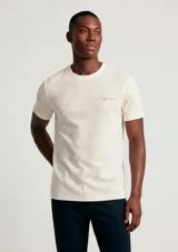 Remera manga corta de color blanco con sutiles vetas, cuello redondo y un pequeño bordado en el pecho.