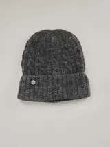 Gorro de lana tejido en punto grueso, color gris jaspeado, con borde doblado y aplique metálico circular con logo de la marca.