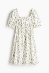 Vestido corto de color blanco con estampado floral en tonos morados, escote cuadrado, mangas cortas abullonadas y cuerpo fruncido elástico.
