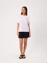 Remera blanca de corte holgado, con cuello redondo y mangas cortas. Presenta un pequeño estampado en el pecho con diseño floral y tipografía.