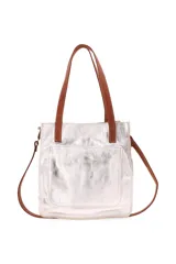 Bolso de cuero con acabado metalizado plateado y detalles en cuero color suela. Cuenta con doble asa corta para llevar al hombro y una correa larga ajustable y extraíble. Presenta un bolsillo frontal externo y cierre principal.