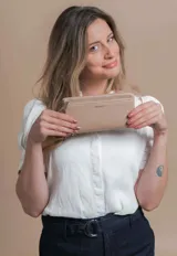 Billetera de mujer tipo sobre con correa de mano extraíble, confeccionada en material texturizado color tostado. Presenta un bolsillo frontal con cierre, compartimentos internos para tarjetas y logo de la marca grabado en el frente.