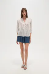 Camisa de algodón con diseño de rayas verticales y detalles bordados. Presenta cuello en V, cierre frontal con botones y mangas tres cuartos con terminación elástica.