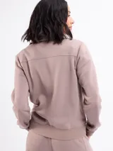 Campera de felpa con cierre frontal completo, cuello alto y bolsillos laterales. Presenta puños y ruedo acanalados, con costuras decorativas que definen la silueta.