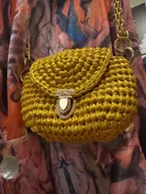 Cartera de mano tejida color dorado, con cierre metálico y cadena gruesa dorada.