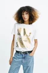 Camiseta de cuello redondo y manga corta con estampado metalizado dorado y texto a contraste en el frente.