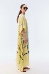 Kaftan maxi amplio de color amarillo, con escote redondo, mangas cortas y ruedo irregular. Presenta un diseño estampado a cuadros con efecto teñido.