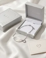 Pulsera de cadena tipo rolo en acero, con placa ovalada central grabada con la frase 'Te quiero Mamá' y dijes de corazón en los extremos.