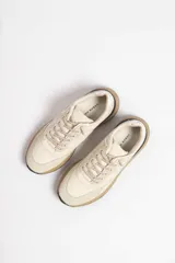 Zapatillas deportivas color crema con detalles en beige, negro y blanco.