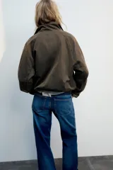 Chaqueta encerada color marrón con efecto lavado, cuello subido y manga larga. Cuenta con bolsillos frontales de plastrón y cierre de cremallera oculto por solapa con botones a presión. Los puños reversibles dejan ver un forro interior con estampado a cuadros.
