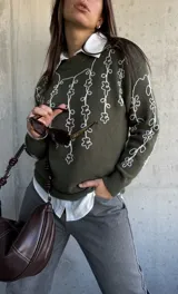 Sweater de punto color verde oliva con cuello redondo y diseño de flores bordadas en hilo blanco en el frente y las mangas.