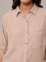 Camisa color beige de algodón y lino, con cuello clásico, cierre frontal con botones, mangas largas con puños abotonados, dos bolsillos con solapa en el pecho y corte holgado.