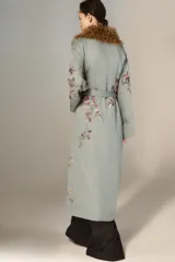 Kimono de largo midi en color verde grisáceo, con cuello de solapas amplias en pelo sintético marrón. Presenta mangas largas acampanadas, cierre frontal con cinturón ajustable del mismo tejido y un delicado estampado floral bordado en toda la prenda.