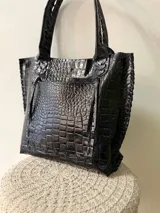 Cartera tipo shopper de cuero genuino marrón, con terminaciones artesanales trenzadas en las asas y los laterales, bolsillo frontal externo y asas largas para llevar al hombro.