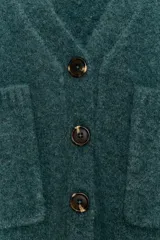 Chaqueta de punto de textura suave en color marrón oscuro, con escote en pico, manga larga y cierre frontal con botones. Presenta dos bolsillos de plastrón en la parte delantera.