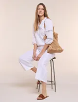 Pantalón crop de lino y algodón color blanco, con calce holgado, pierna ancha de corte recto y cintura elástica. Presenta bolsillos laterales y detalle de puntilla aplicada en el frente.