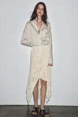 Falda midi color crudo, de tiro medio y confeccionada en viscosa. Presenta detalle de pliegues y bajo asimétrico. Cierre lateral con cremallera oculta.