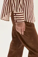 Camisa de manga larga con cuello y puños, confeccionada en tejido de rayas verticales en tonos crema y bordó. Presenta un bolsillo de parche en el pecho con un bordado exclusivo.