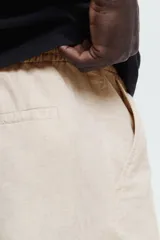 Pantalón de corte regular fit confeccionado en mezcla de lino y algodón, color beige. Presenta cintura elástica con cordón ajustable, cierre de botón y bolsillos laterales.