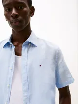 Camisa celeste de lino con corte regular, manga corta, cuello abotonado y logo de Tommy Hilfiger bordado en el pecho.