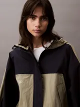 Campera corta con capucha, confeccionada en tejido ripstop de nailon en dos tonos: beige y negro. Tiene corte relaxed, cierre de cremallera y botón de presión, bolsillos con cremallera en la cintura, bajo con cordón elástico, forro de malla transpirable y logo CK bordado en el pecho.