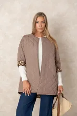 Campera acolchada de corte amplio y largo midi, color beige con diseño capitoneado. Presenta mangas tres cuartos con puños vueltos que revelan un interior estampado con motivo animal print. Diseño sin cuello y cierre frontal oculto.