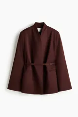 Blazer oversized bordó de cuello alto, con hombreras, bolsillos delanteros ribeteados, abertura en los puños y cinturón fino incorporado con hebilla metálica.