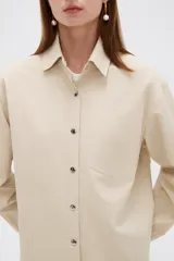 Campera marrón de manga larga confeccionada en algodón, con cuello camisero, cierre frontal con botones a presión y puños elásticos fruncidos.